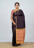 Traditional Indian woman posing in a deep wine-black Kanchi soft silk saree featuring a peach-gold zari border and matching peach blouse