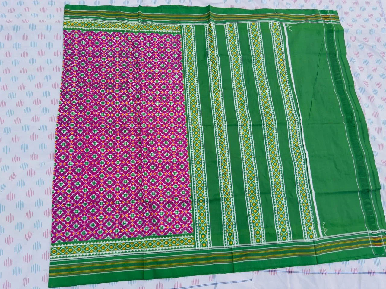 Flat lay of an authentic double ikat patola silk saree with a magenta geometric patterned body, bold green striped pallu, and Silk Mark certification