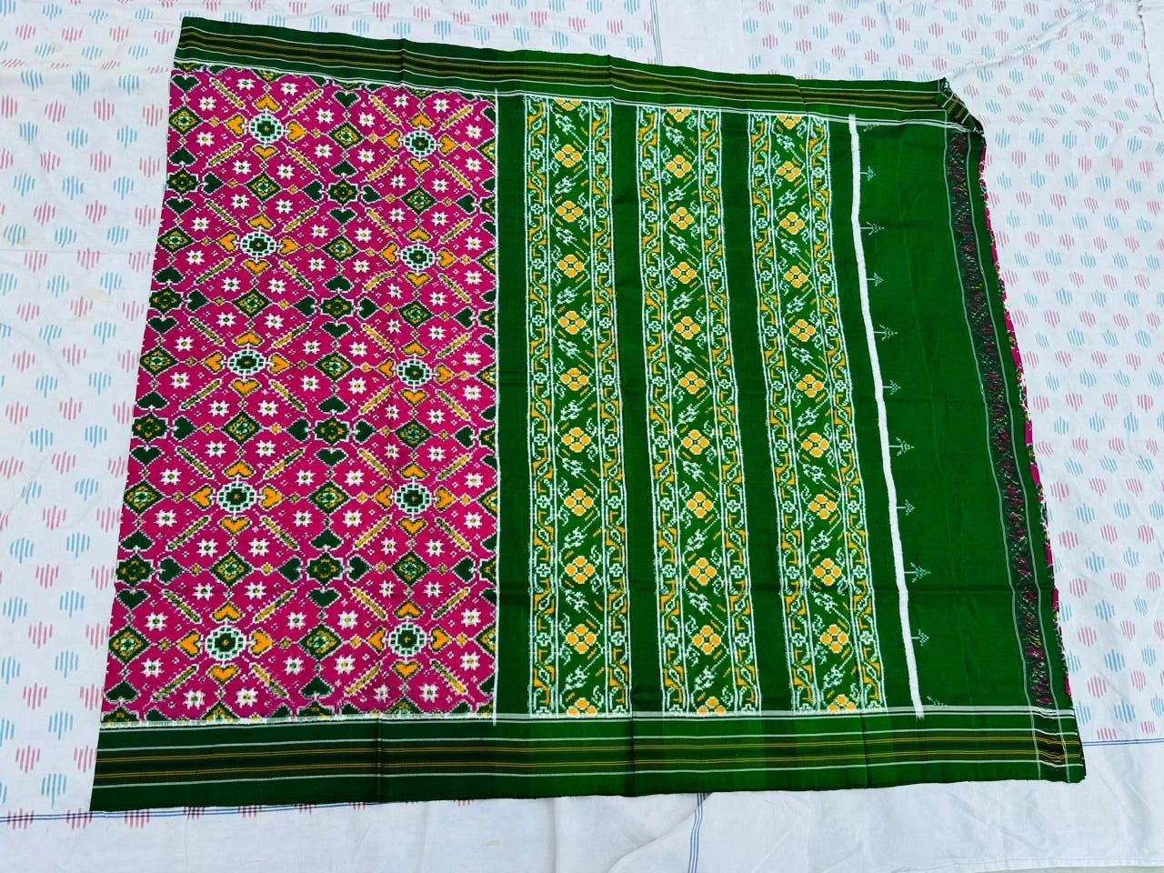 Flat lay of an authentic double ikat patola silk saree with a magenta geometric patterned body, bold green striped pallu, and Silk Mark certification