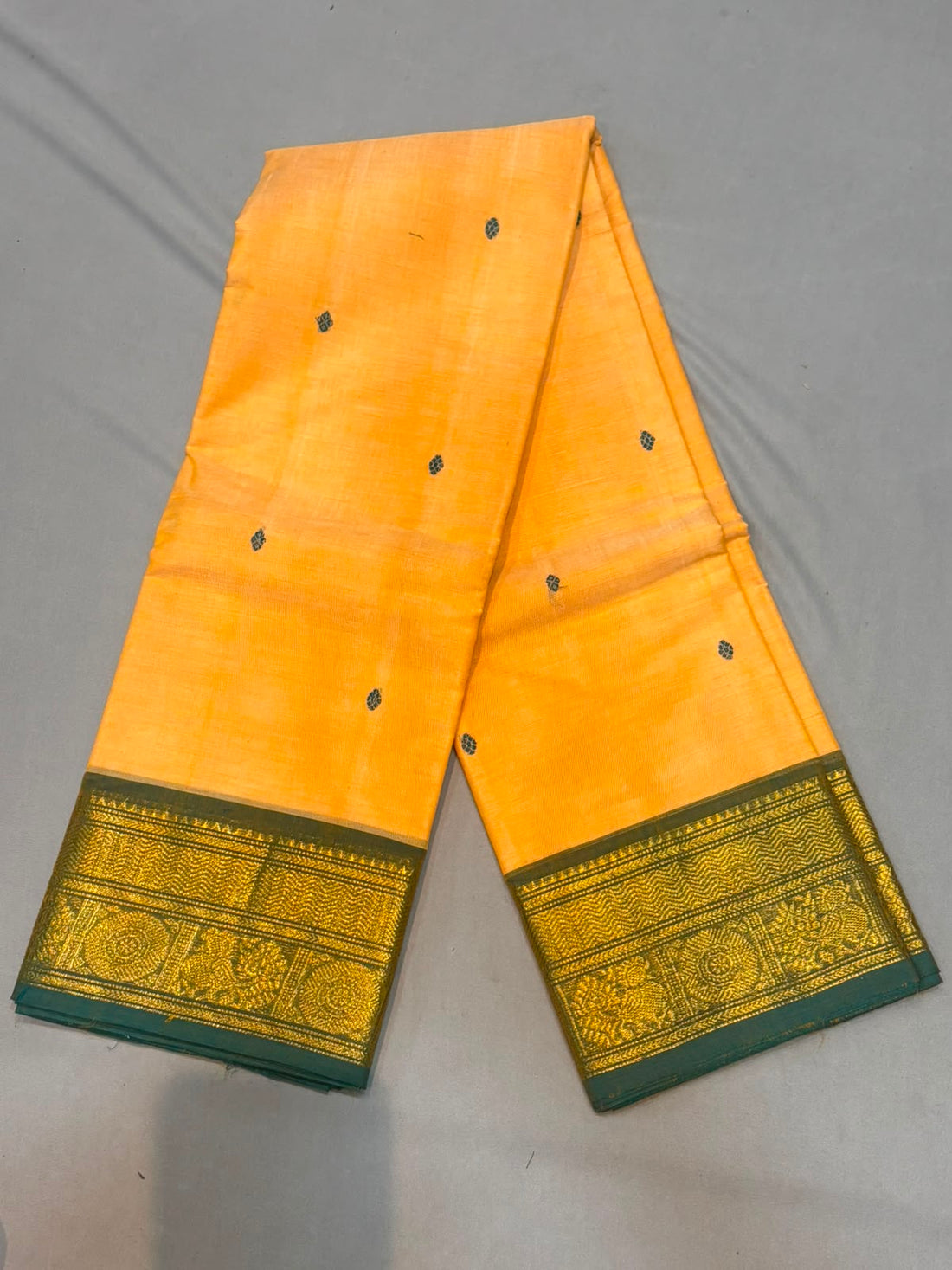 Mango yellow Kanchi cotton saree featuring small woven buttas and an ornate green and gold zari border with matching running blouse piece.