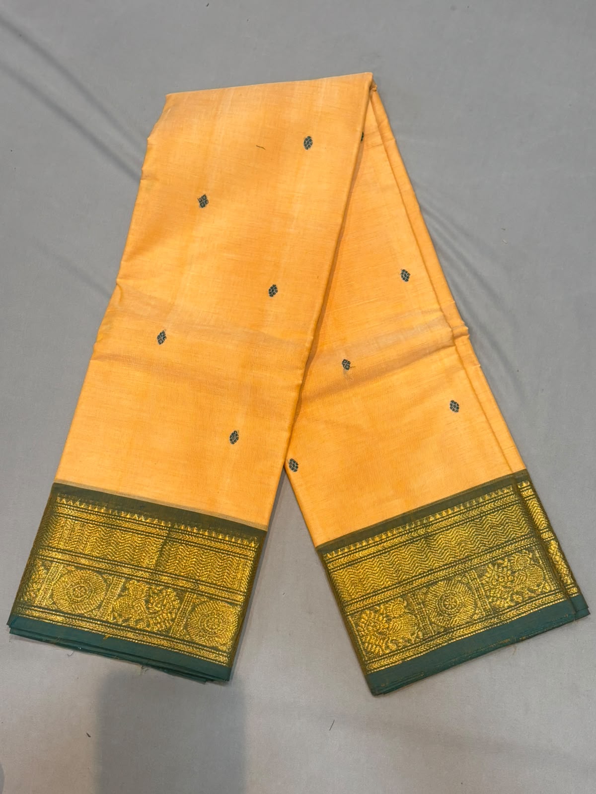Mango yellow Kanchi cotton saree featuring small woven buttas and an ornate green and gold zari border with matching running blouse piece.
