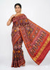 A beautiful Indian woman standing elegantly against a white background, draped in a pure Patola silk saree. She is showcasing the deep maroon body with woven lion, elephant, and butterfly Ikat motifs, along with the rich red pallu featuring traditional floral and geometric patterns.