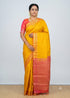 A traditional Indian woman drapes an elegant mustard yellow Kanchi soft silk saree featuring a contrasting coral-pink gold zari border and pallu, standing against a plain white background.