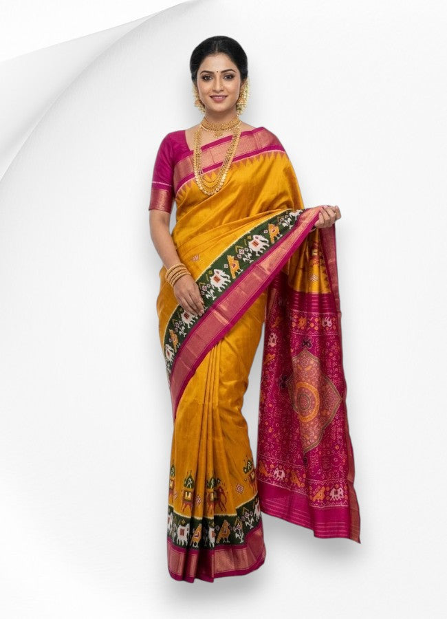 A woman modeling a traditional mustard yellow silk saree featuring a dark green border with elephant motifs and a richly patterned pink and magenta pallu.