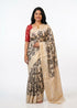 A woman smiling while modeling an elegant off-white Ikat silk saree with black patterns and a contrast red blouse.