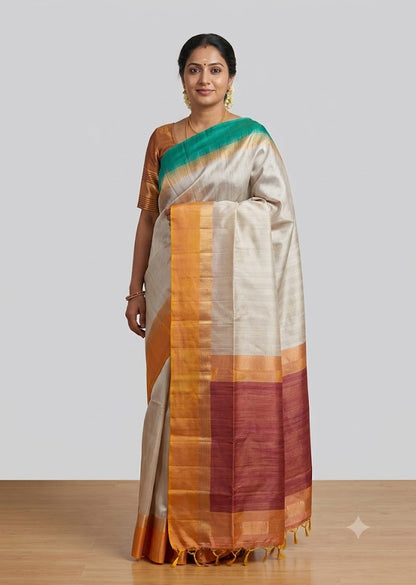 Model posing in an off-white traditional silk saree with a gold-yellow border, teal green pallu accent, and matching golden blouse.