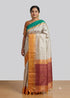 Model posing in an off-white traditional silk saree with a gold-yellow border, teal green pallu accent, and matching golden blouse.