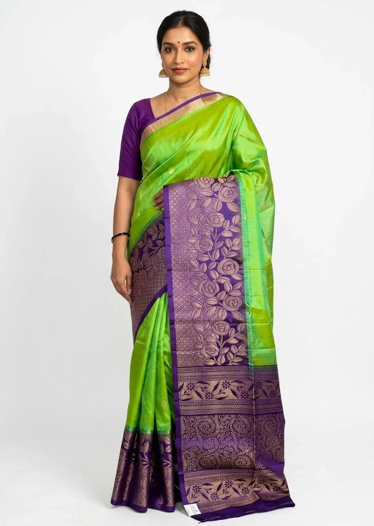 Model showcasing the front view of a parrot green Kanchi soft silk saree with a broad purple gold zari floral border.