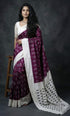 Indian woman standing wearing a rich plum purple handloom ikkat silk saree with a broad off-white border and traditional jewelry