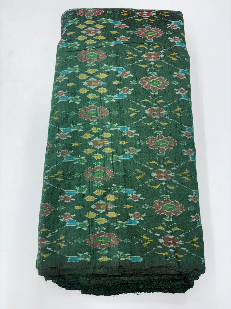 Folded bolt of bottle green pure raw silk fabric featuring vibrant multicolor floral Ikat motifs with Silk Mark quality weave