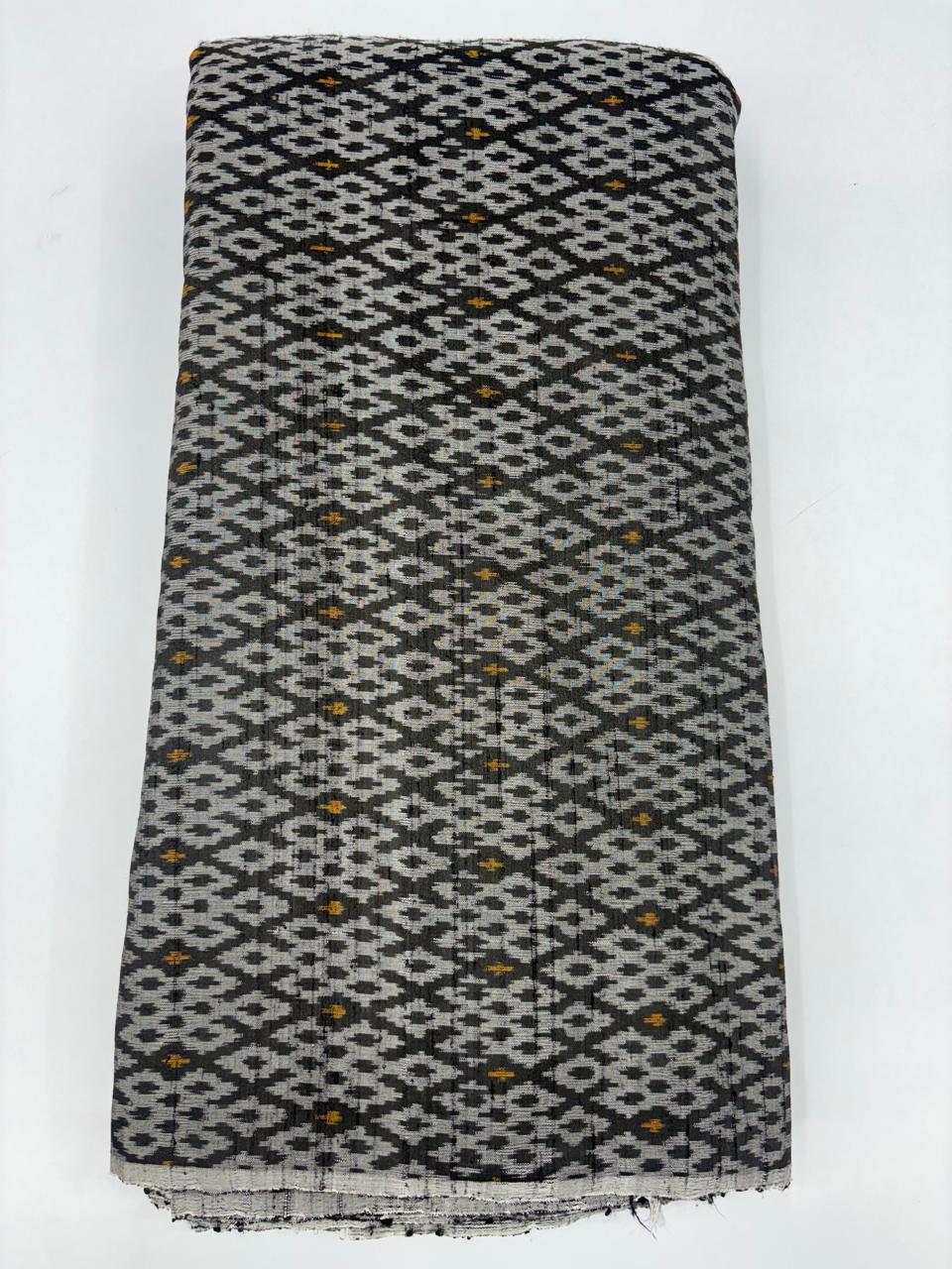 Folded bolt of charcoal black pure raw silk fabric featuring an intricate geometric diamond Ikat weave with Silk Mark authenticity.