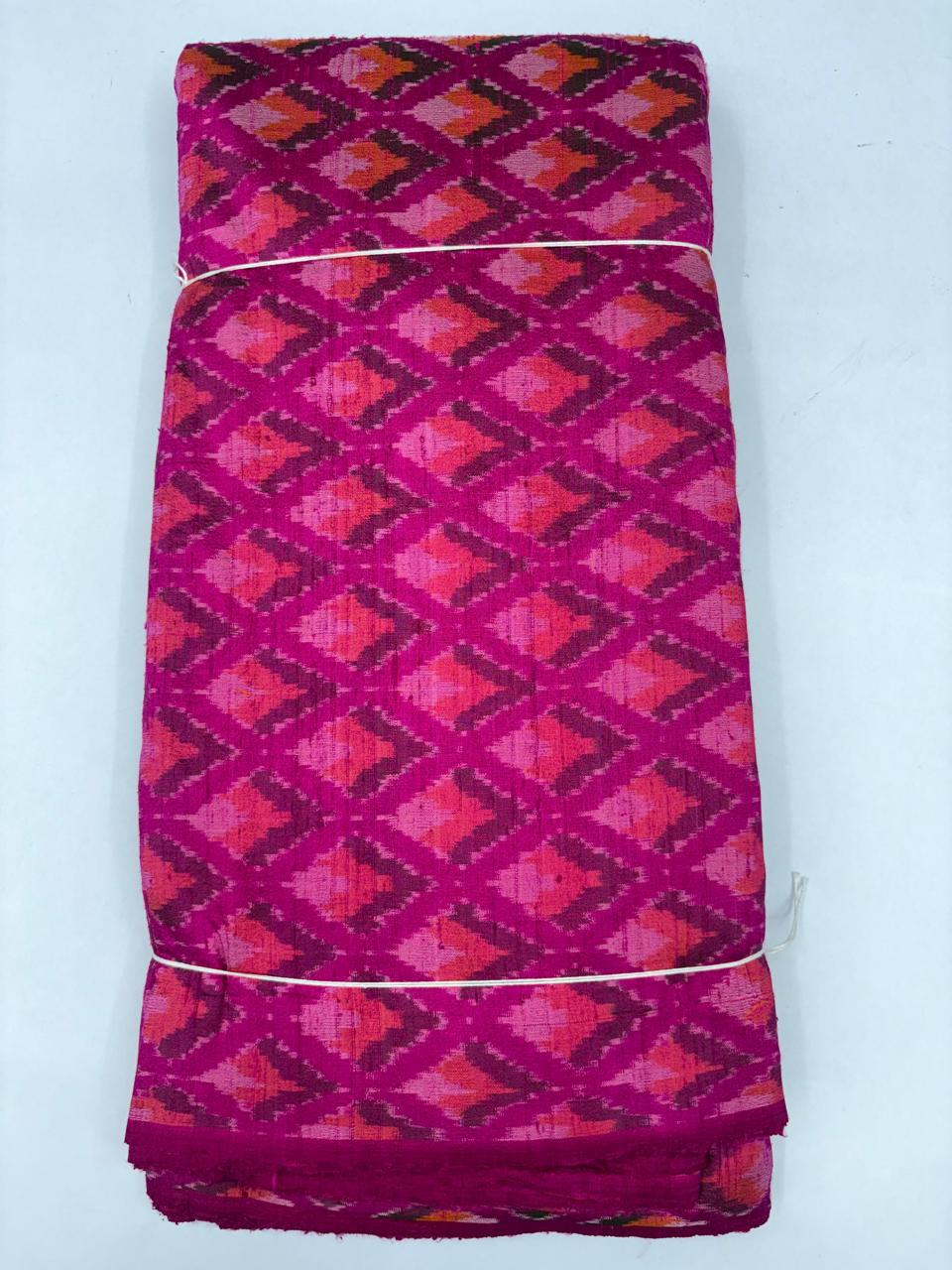 Folded bolt of vibrant magenta pink pure raw silk fabric featuring geometric diamond Ikat motifs and Silk Mark quality weave