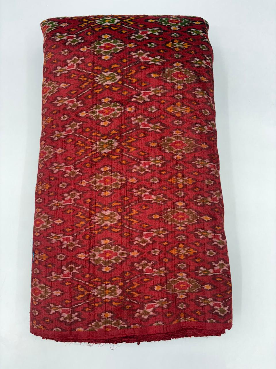 Folded bolt of maroon red pure raw silk fabric featuring an intricate multicolor floral diamond Ikat weave with Silk Mark authenticity