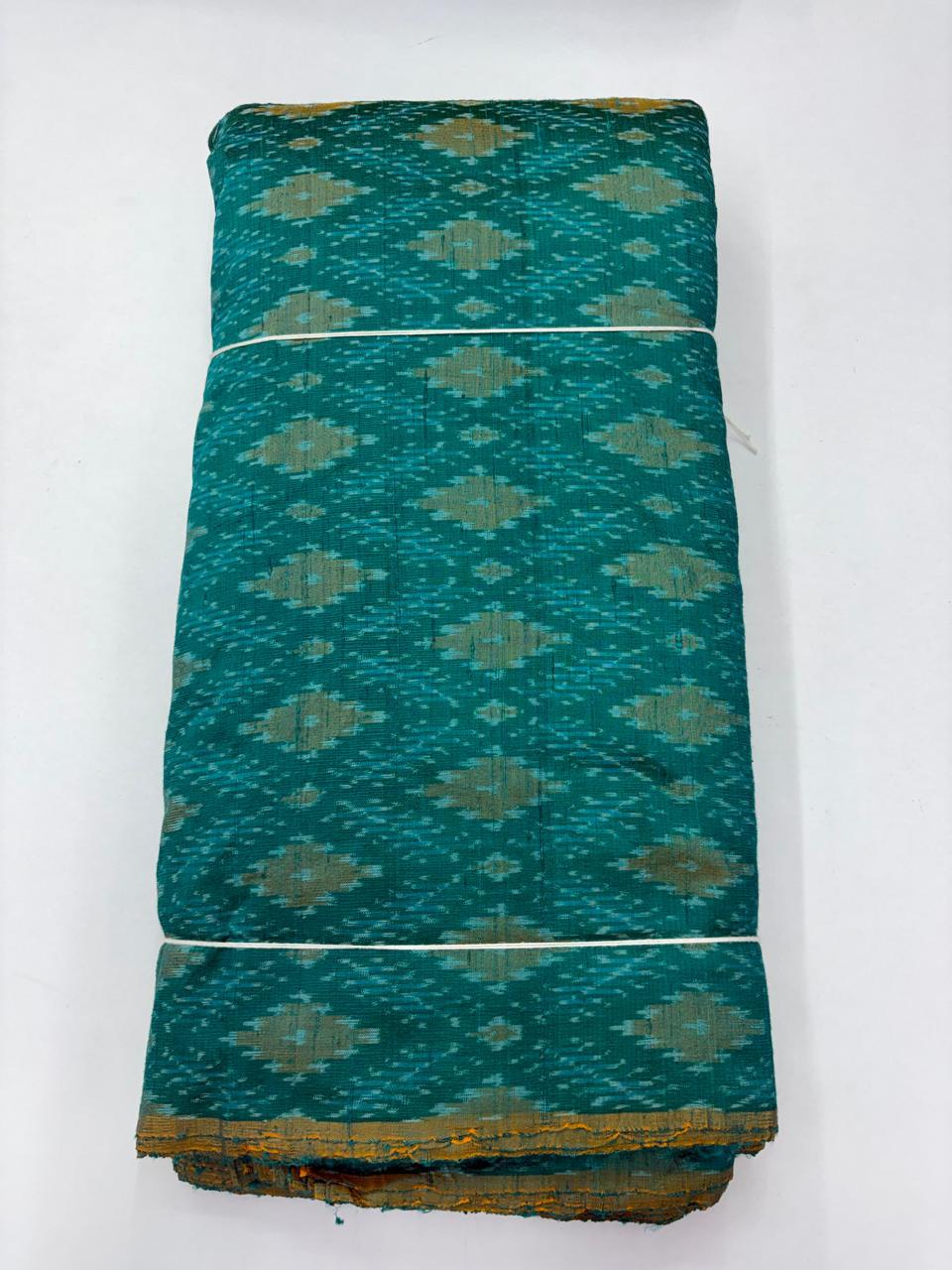 Folded bolt of teal green pure raw silk fabric featuring traditional geometric diamond Ikat motifs and Silk Mark quality weave