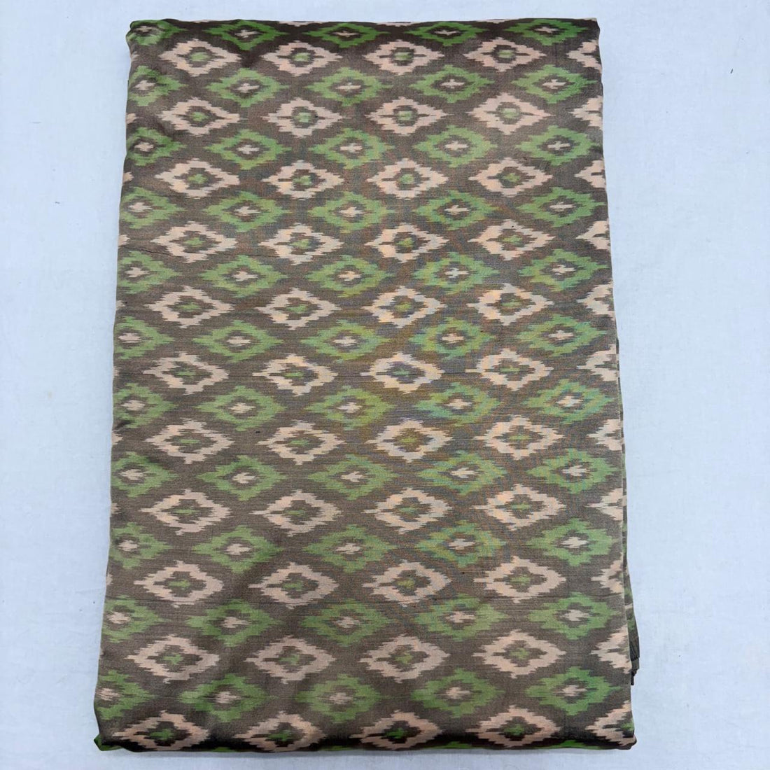 Folded charcoal grey pure silk Ikat fabric featuring alternating olive green and beige geometric diamond motifs with Silk Mark certification