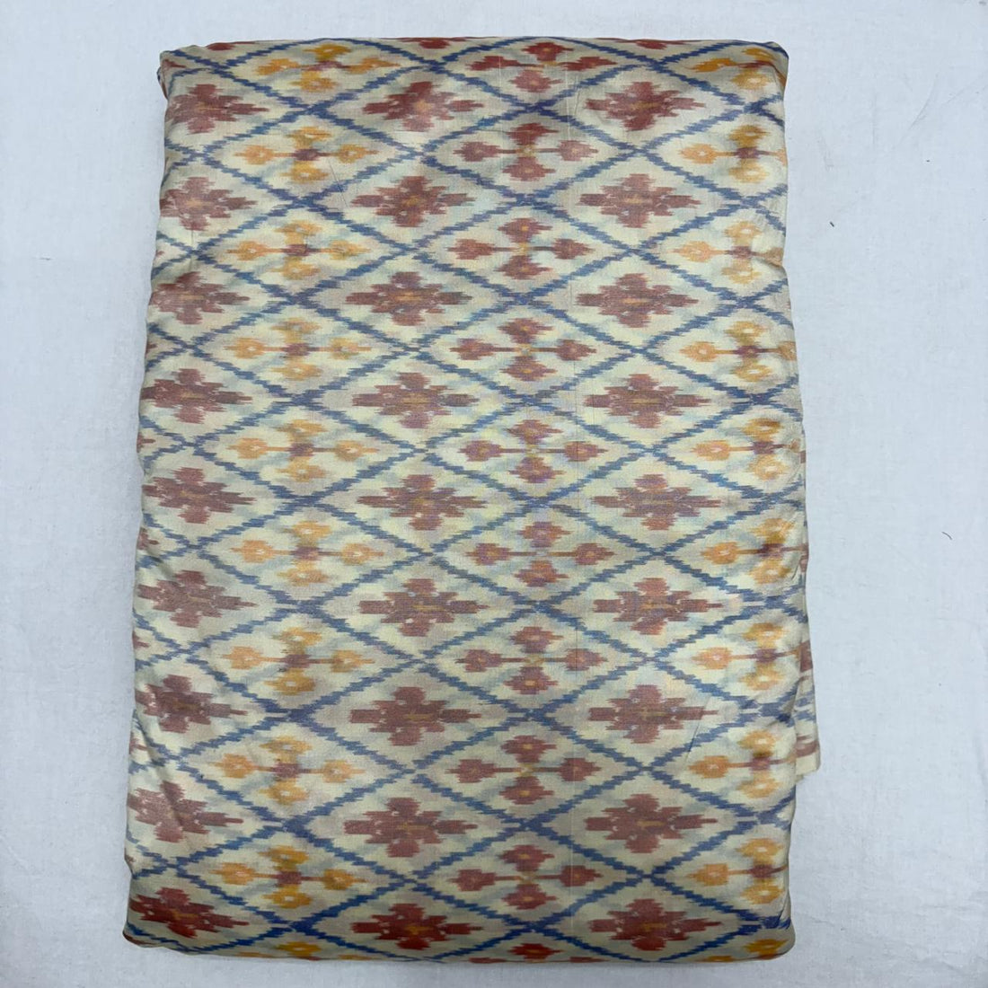 Folded ivory cream pure silk Ikat fabric featuring slate blue geometric diamond lattice with terracotta rust and mustard motifs with Silk Mark certification