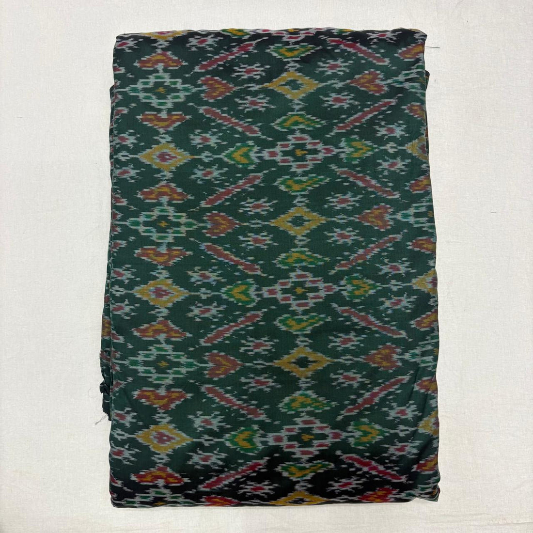 Folded deep forest green pure silk Ikat fabric featuring traditional geometric diamond and rust motifs with Silk Mark certification.