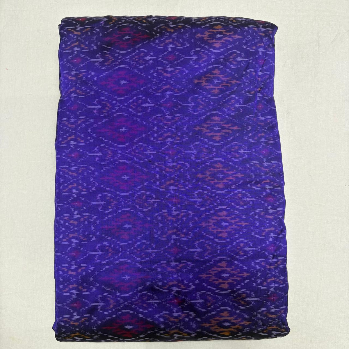 Folded deep indigo purple pure silk Ikat fabric featuring geometric diamond lozenge patterns in magenta and plum with Silk Mark certification.