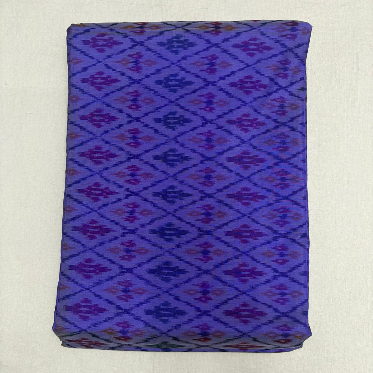 Folded indigo violet pure silk Ikat fabric featuring geometric diamond trellis lattice in plum purple and magenta with Silk Mark certification.