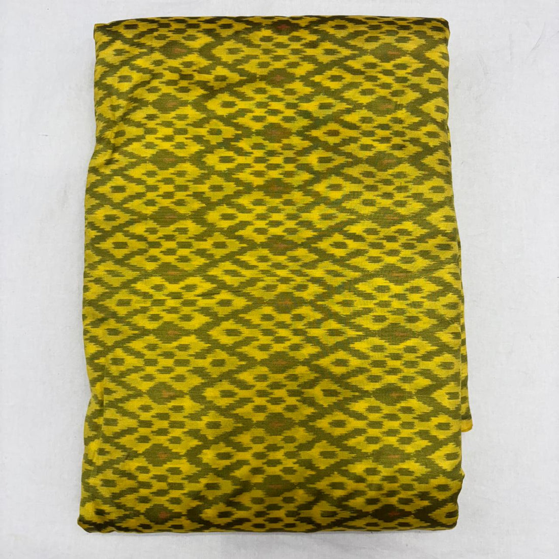 Folded mustard yellow pure silk Ikat fabric featuring olive green geometric diamond motifs with Silk Mark certification.