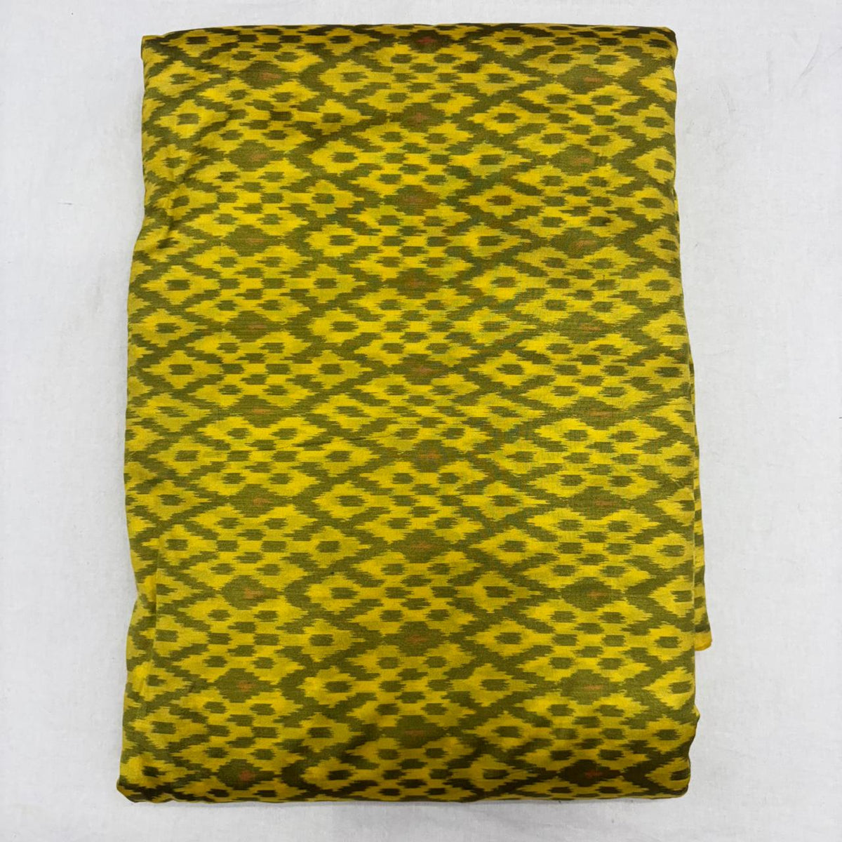 Folded mustard yellow pure silk Ikat fabric featuring olive green geometric diamond motifs with Silk Mark certification.