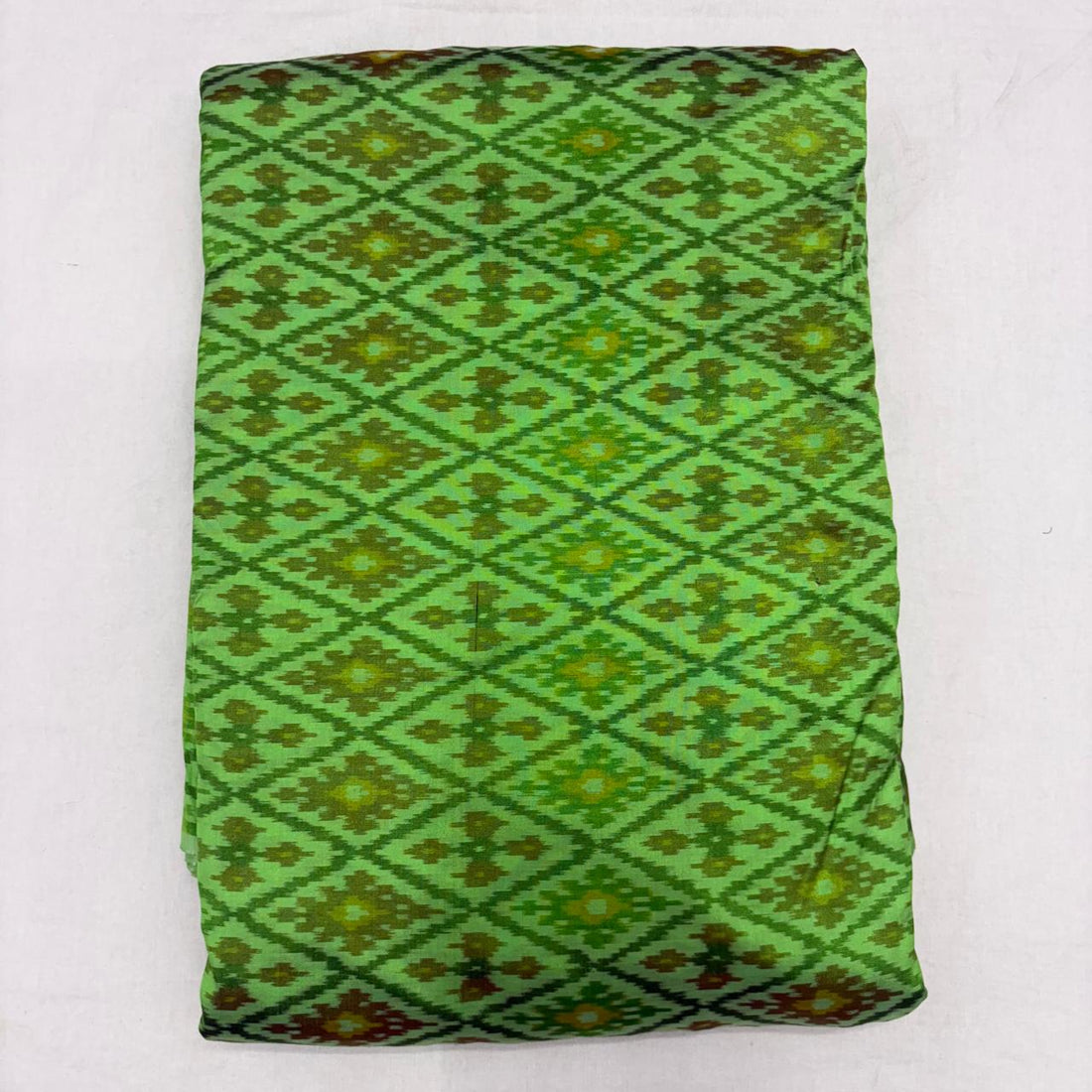 Folded vibrant parrot green pure silk Ikat fabric featuring intricate geometric diamond and olive floral motifs with Silk Mark certification.