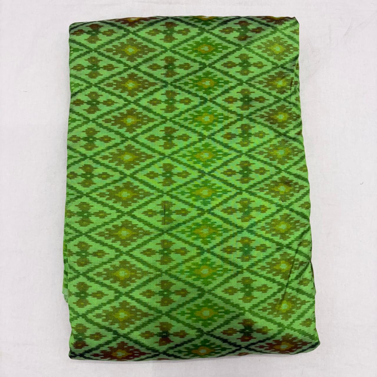Folded vibrant parrot green pure silk Ikat fabric featuring intricate geometric diamond and olive floral motifs with Silk Mark certification.