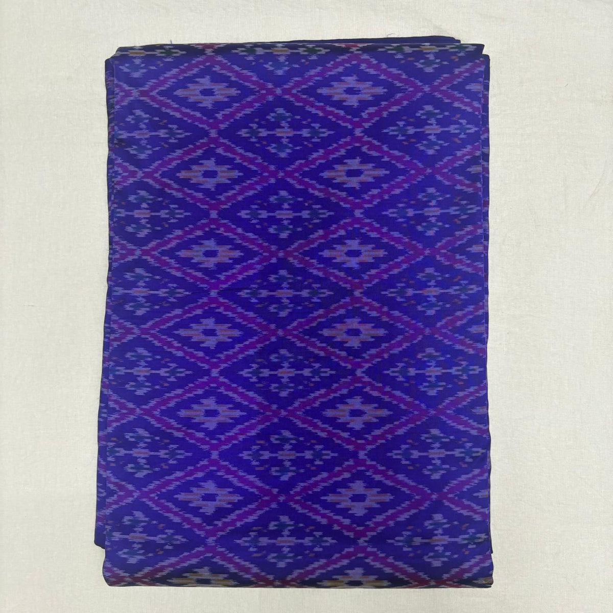 Folded royal blue pure silk Ikat fabric featuring geometric diamond lattice patterns in purple and soft lavender with Silk Mark certificatio