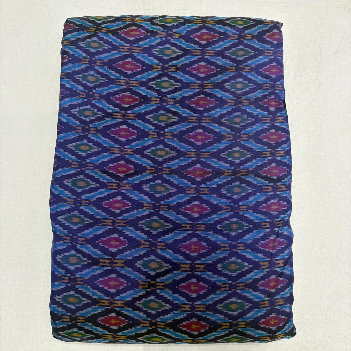  Folded royal blue pure silk Ikat fabric featuring sky blue geometric diamond lattice with magenta and olive motifs with Silk Mark certification.