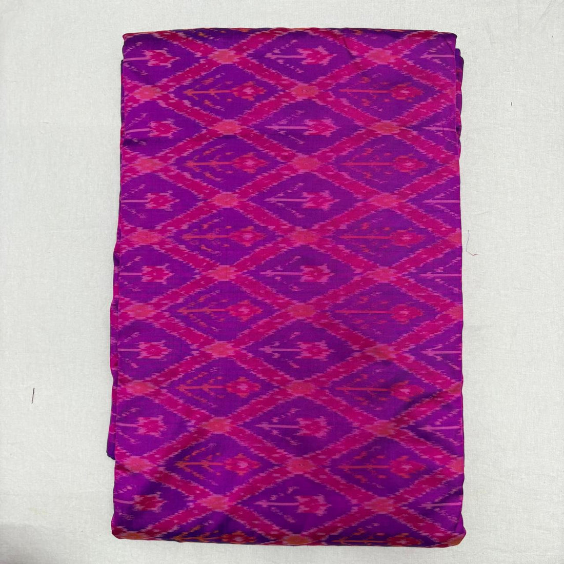Folded royal purple pure silk Ikat fabric featuring vibrant magenta geometric diamond trellis patterns with Silk Mark certification.