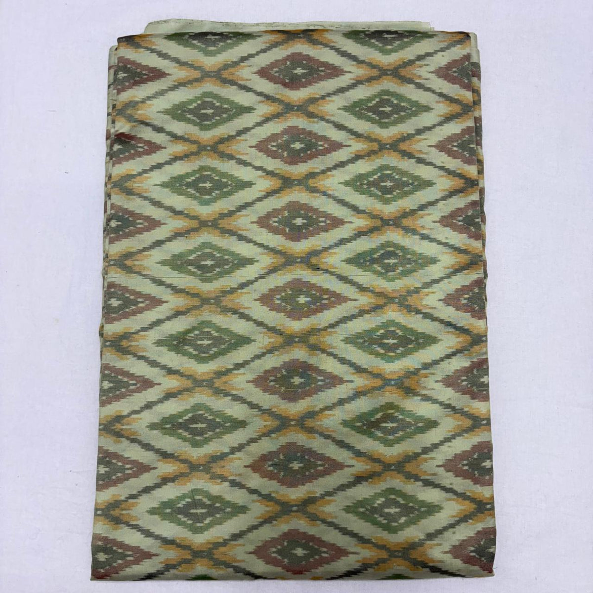 Folded pale sage cream pure silk Ikat fabric featuring olive green, mustard yellow, and rust geometric diamond patterns with Silk Mark certification