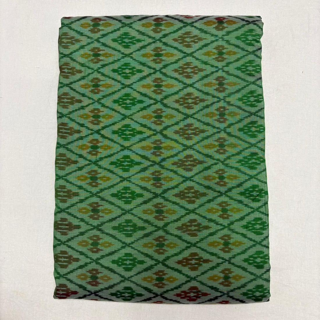 Folded mint sea green pure silk Ikat fabric featuring geometric diamond lattice with olive brown and mustard motifs with Silk Mark certification.   