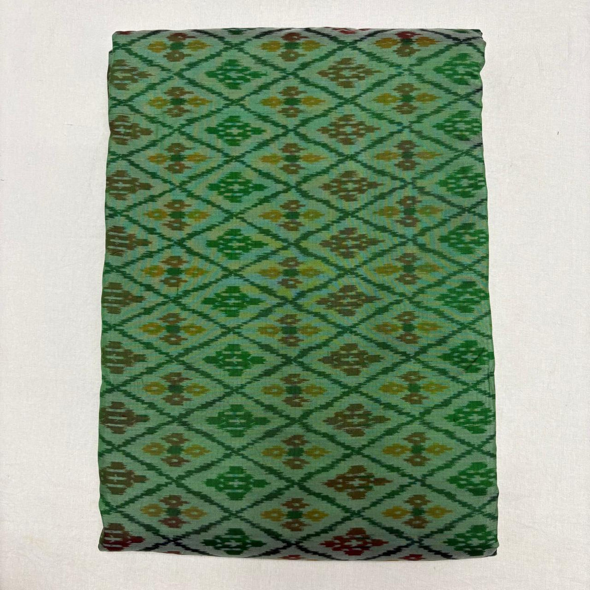 Folded mint sea green pure silk Ikat fabric featuring geometric diamond lattice with olive brown and mustard motifs with Silk Mark certification.   