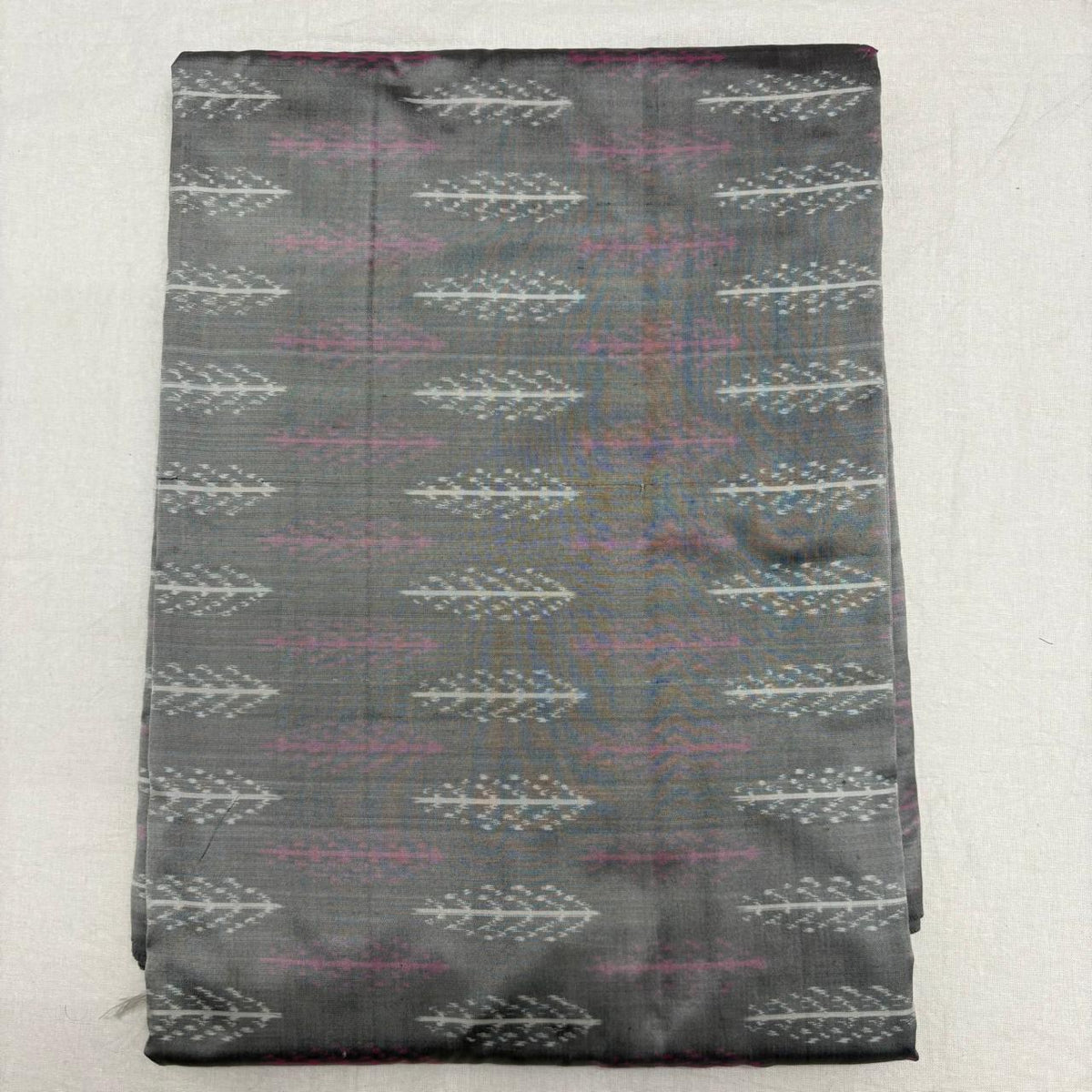 Folded slate grey pure silk Ikat fabric featuring linear silver-white leaf motifs and muted mauve accents with Silk Mark certification