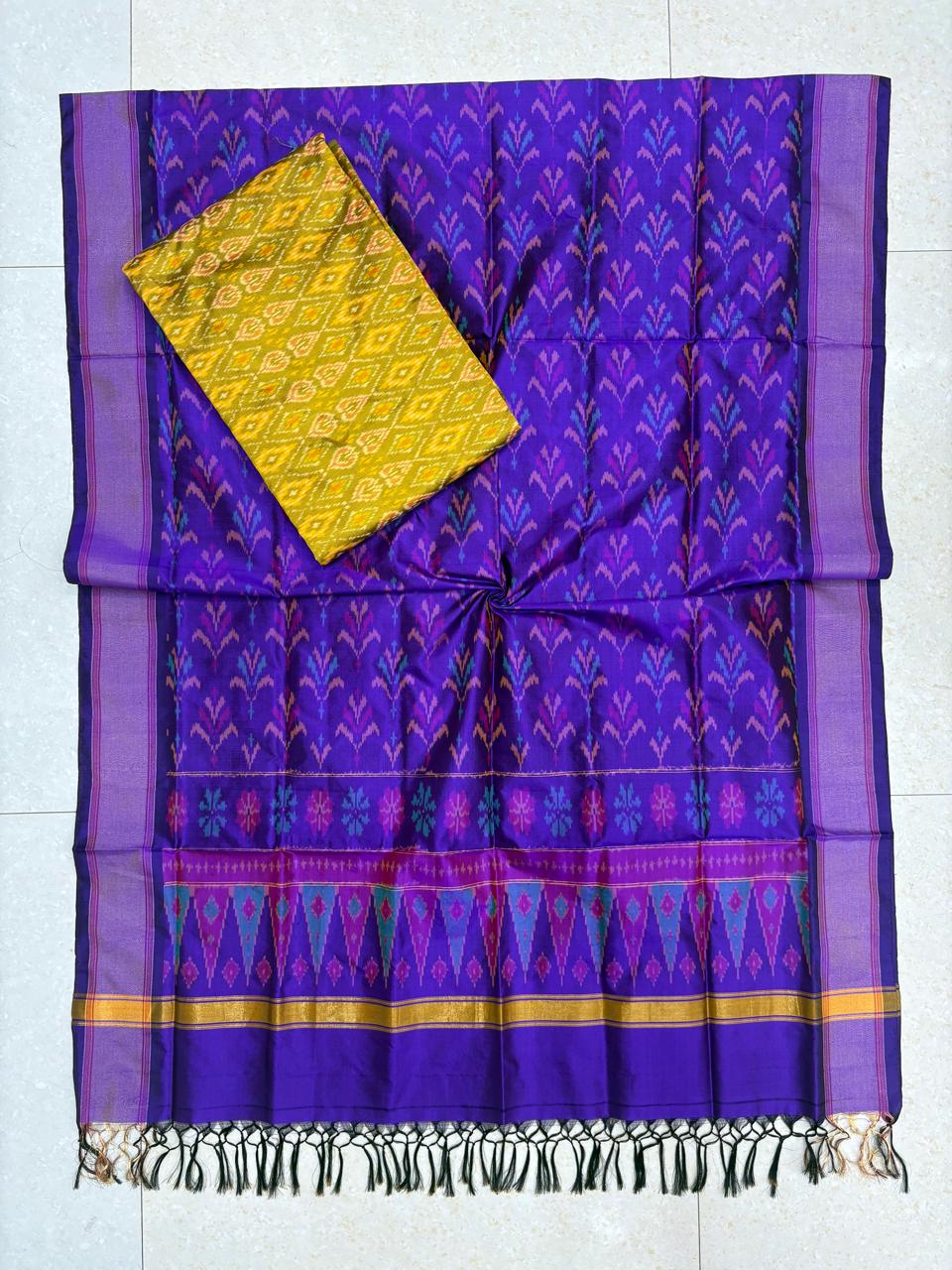 Deep purple and mustard yellow Pochampally Ikat silk unstitched dress material set featuring handwoven floral motifs, a geometric patterned top, a multi-colored temple border, and knotted tassels.