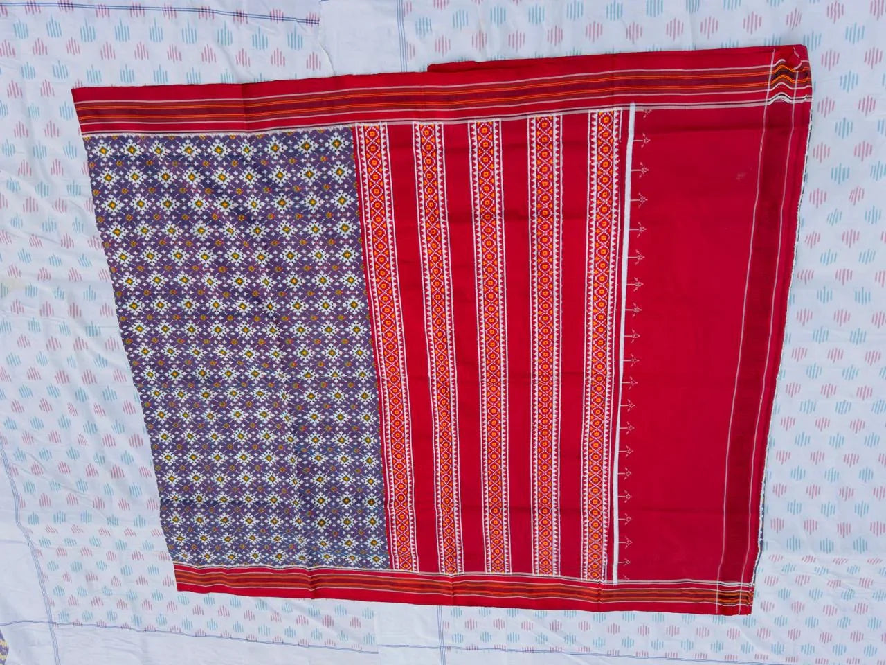 Flat lay of an authentic double ikat patola silk saree with a deep purple geometric patterned body, red striped pallu, and Silk Mark certification
