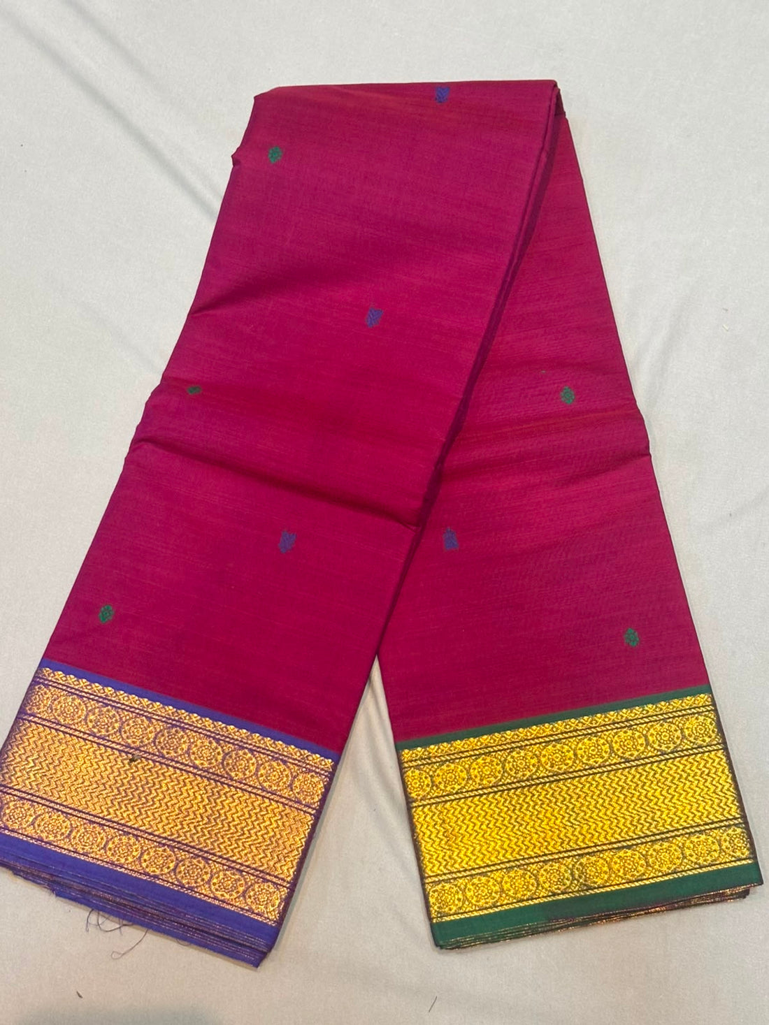 Rani pink Kanchi cotton saree showcasing fine woven buttas and contrasting purple and green gold zari borders with running blouse piece.