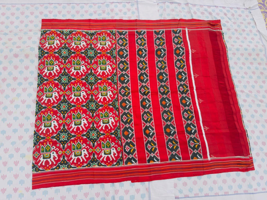 Flat lay of a traditional red Patola silk saree featuring woven elephant and geometric floral motifs with a striped pallu