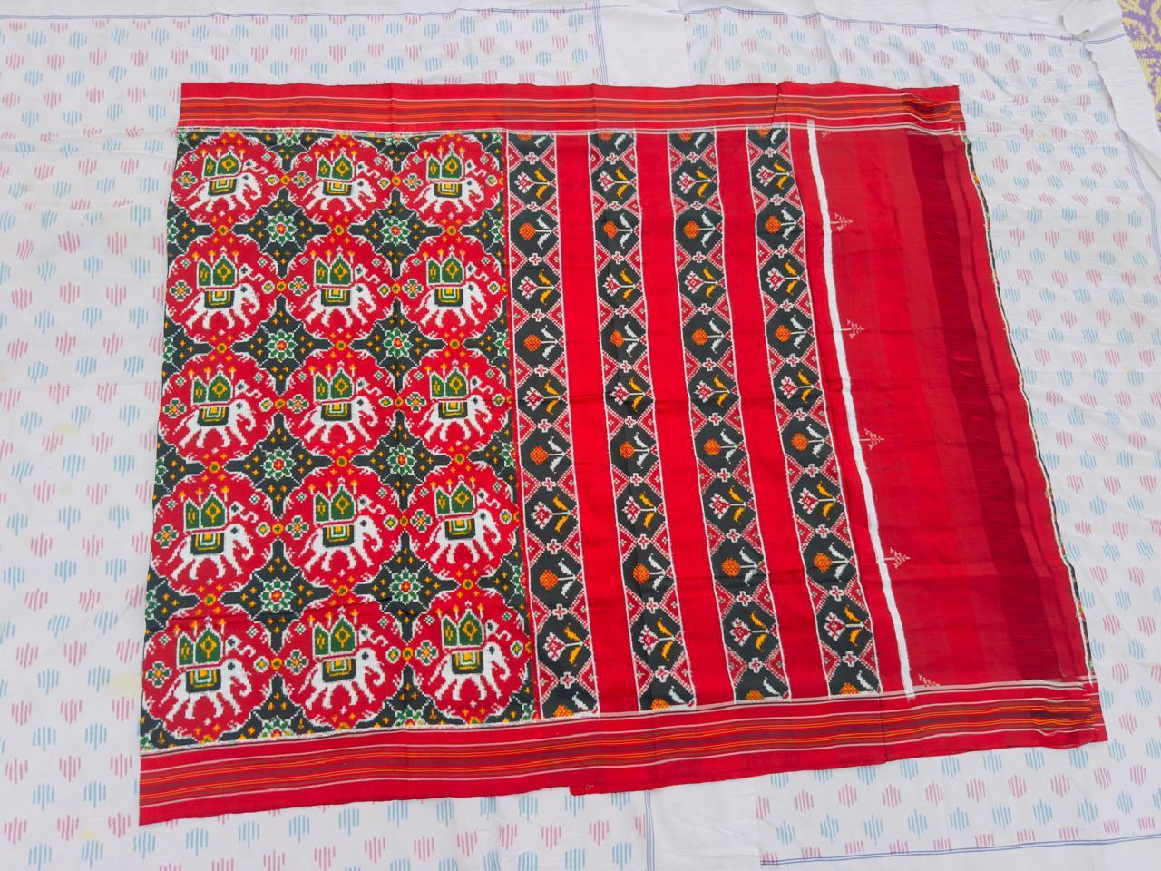 Flat lay of a traditional red Patola silk saree featuring woven elephant and geometric floral motifs with a striped pallu