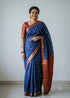 Woman wearing a traditional royal blue Kuppadam Pattu saree with wavy silver and copper zari stripes, copper zari border, and contrast maroon red floral brocade pallu and blouse.