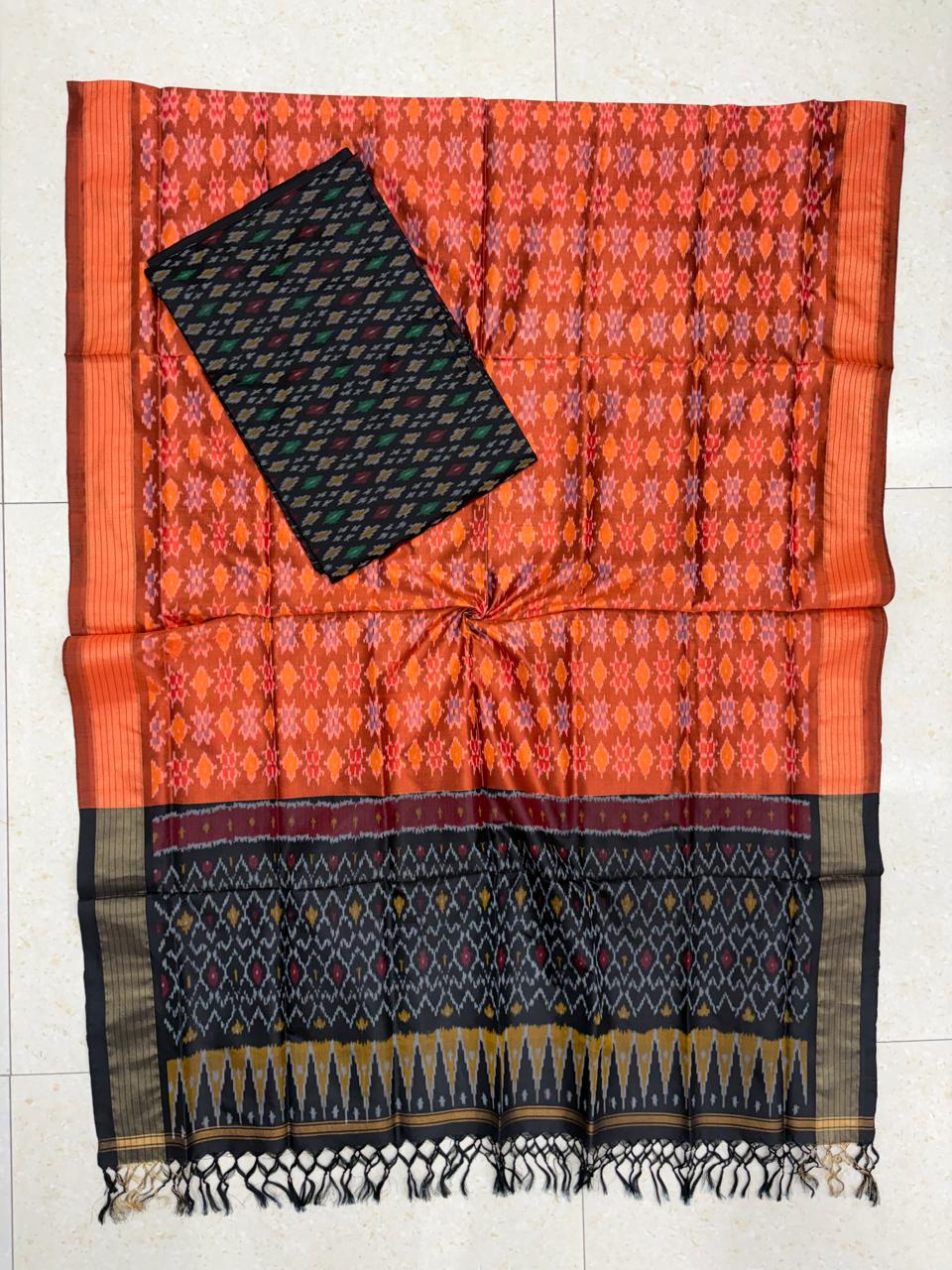 Rust orange and black Pochampally Ikat silk unstitched dress material set featuring handwoven geometric diamond motifs, a detailed black temple pattern border, and black tassels.