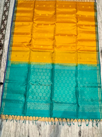Silk Mark certified mustard yellow Kanchi soft silk saree featuring gold coin buttas and a rich peacock teal brocade pallu with tassels