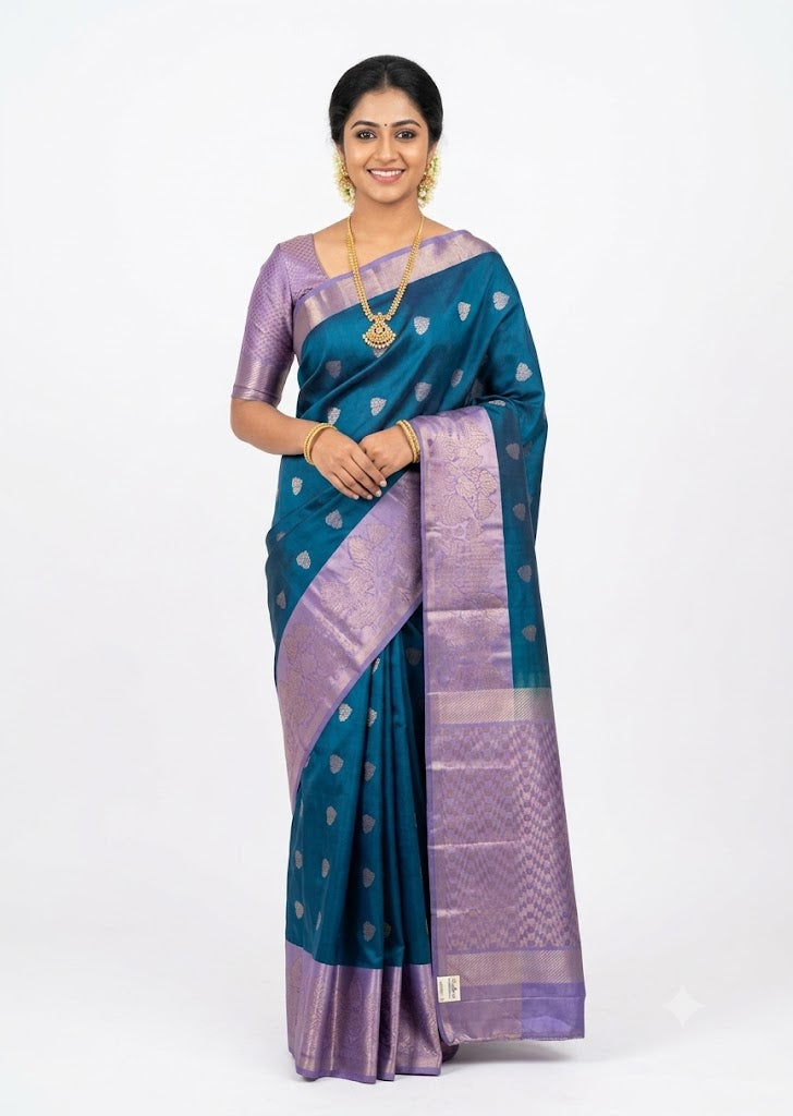 Full view of a teal blue Kanchi soft silk saree displaying intricate leaf motifs on the body and a rich lavender geometric zari pallu.