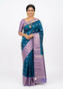 Full view of a teal blue Kanchi soft silk saree displaying intricate leaf motifs on the body and a rich lavender geometric zari pallu.