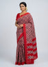 Indian woman posing in a traditional deep crimson red and black Telia Rumal double ikkat handloom cotton saree against a grey studio backdrop.