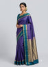 A woman in a traditional pose wearing a violet pure Kanchipuram silk checks saree with a contrasting teal green and gold zari border against a light grey background.