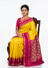 Beautiful traditional Indian woman sitting on a wooden chair wearing a vibrant yellow Pochampally Ikat silk saree featuring a contrast deep pink temple border and geometric patterned pallu, set against a white background.